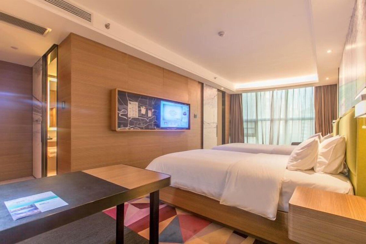 A modern hotel room with a large bed, a desk, and a television mounted on the wall.