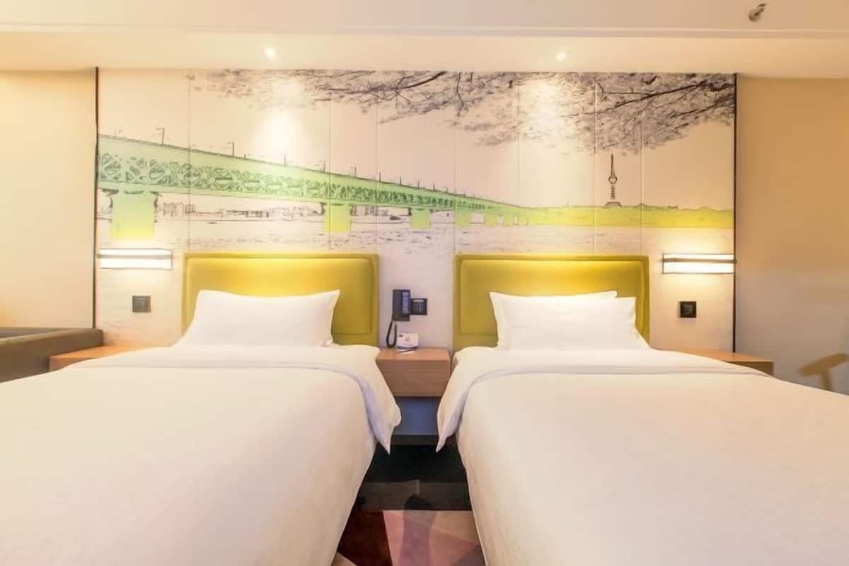 A hotel room with two beds, a mural on the wall, and bedside lamps.