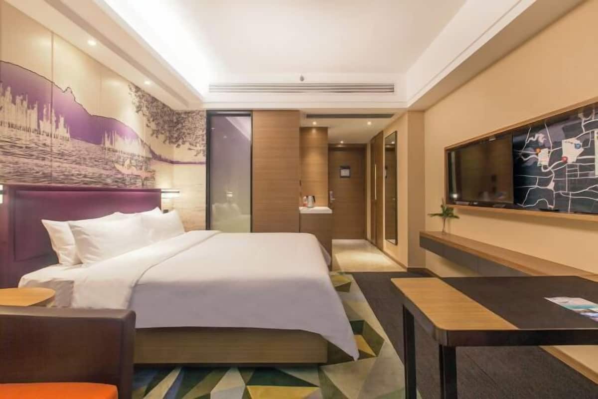 A hotel room with a bed, a desk, a television, and a mural on the wall.