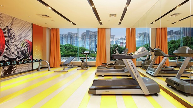 A modern gym with treadmills, a bench, and dumbbells, featuring large windows with a cityscape view. - Hampton by Hilton Wuhan Tianhe Airport East (Wuhan)