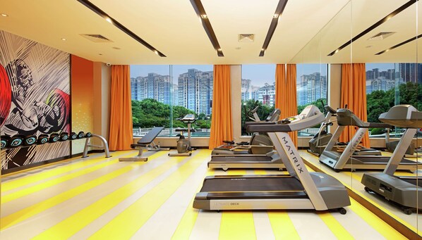 Un gimnasio moderno con cintas de correr, una banca y mancuernas, con amplias ventanas y vista panorámica de la ciudad.
