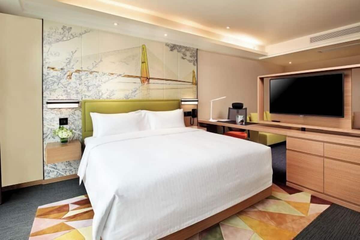 A hotel room with a large bed, a TV, a desk, and a wall with a decorative mural.