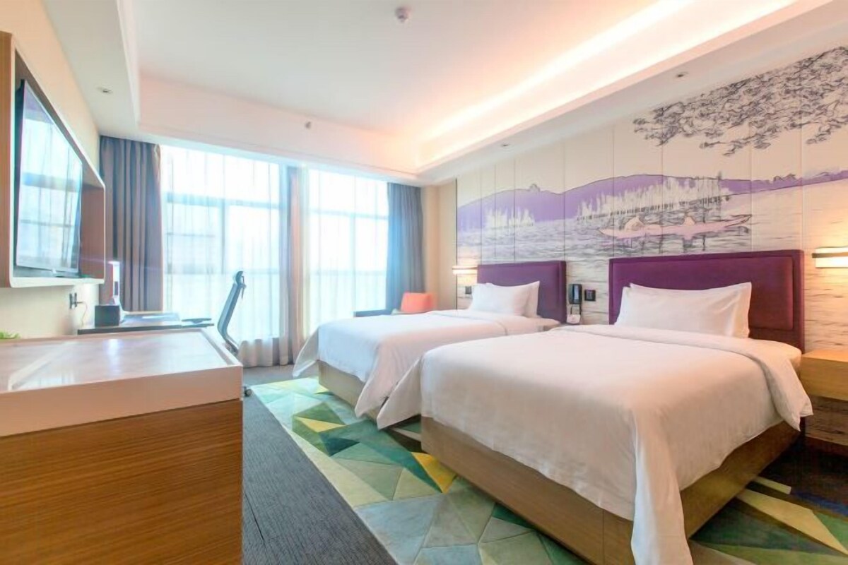 A hotel room with two beds, a desk, a chair, and a large window.