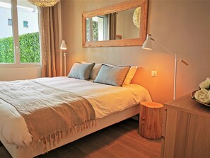 Ein Schlafzimmer mit einem großen Bett, einem Nachttisch aus Holz, einem Spiegel und einem Fenster mit Vorhängen.