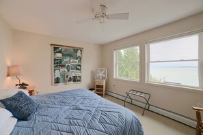 Une chambre à coucher avec un lit, un ventilateur de plafond, une fenêtre donnant sur un beau paysage et un mur orné d’une affiche sur le thème de la faune.