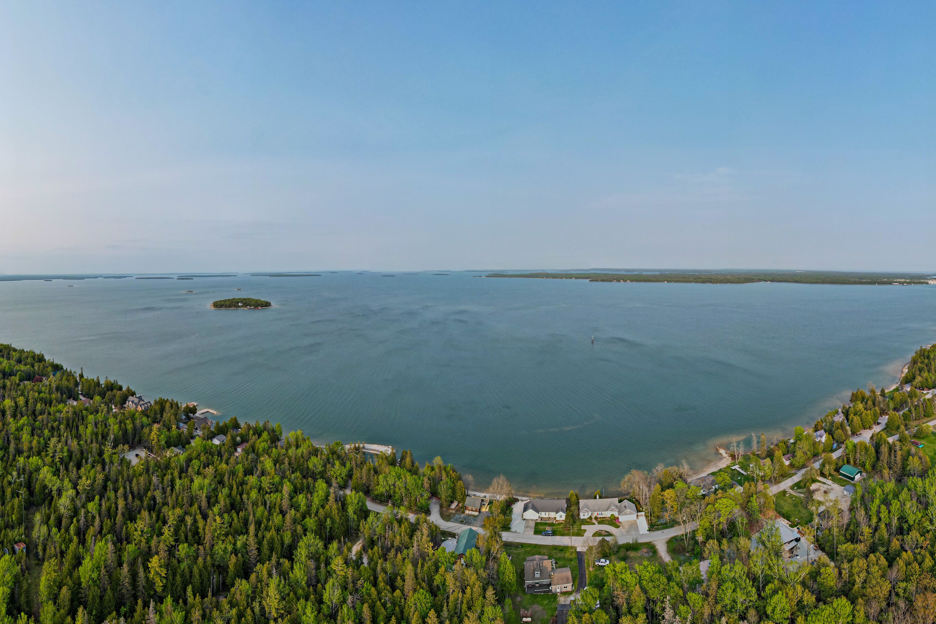 Luchtbeeld van een kustgebied met dicht bos, een klein eiland en helder zicht op het water.