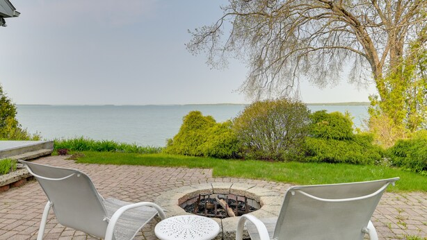 A fire pit with two chairs and a table in a garden area with a view of the lake. - Lakefront De Tour Village Home w/ Deck & Fire Pit! (De Tour Village)