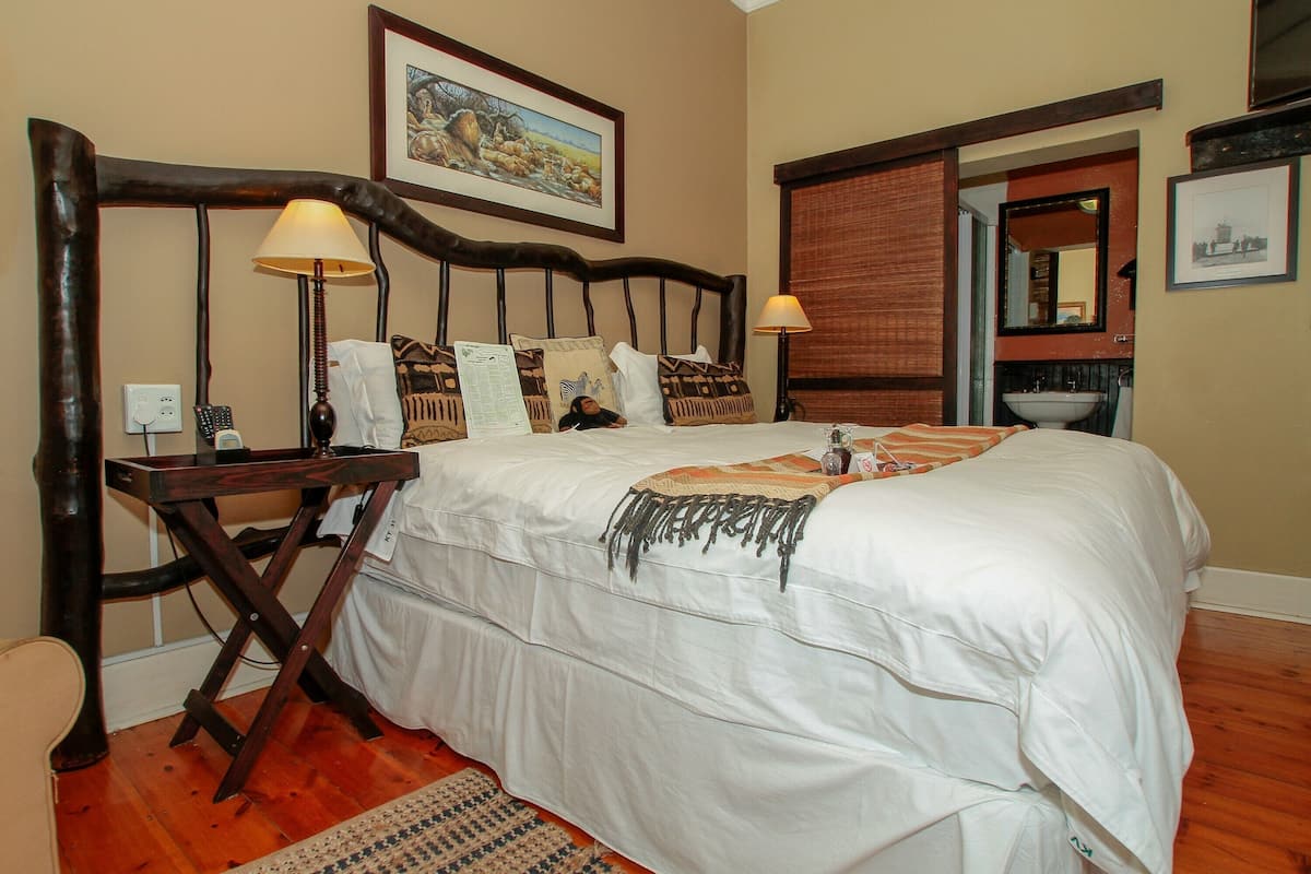A bedroom with a wooden headboard, a bed with white bedding, two bedside lamps, a nightstand, a mirror, and a framed picture on the wall.