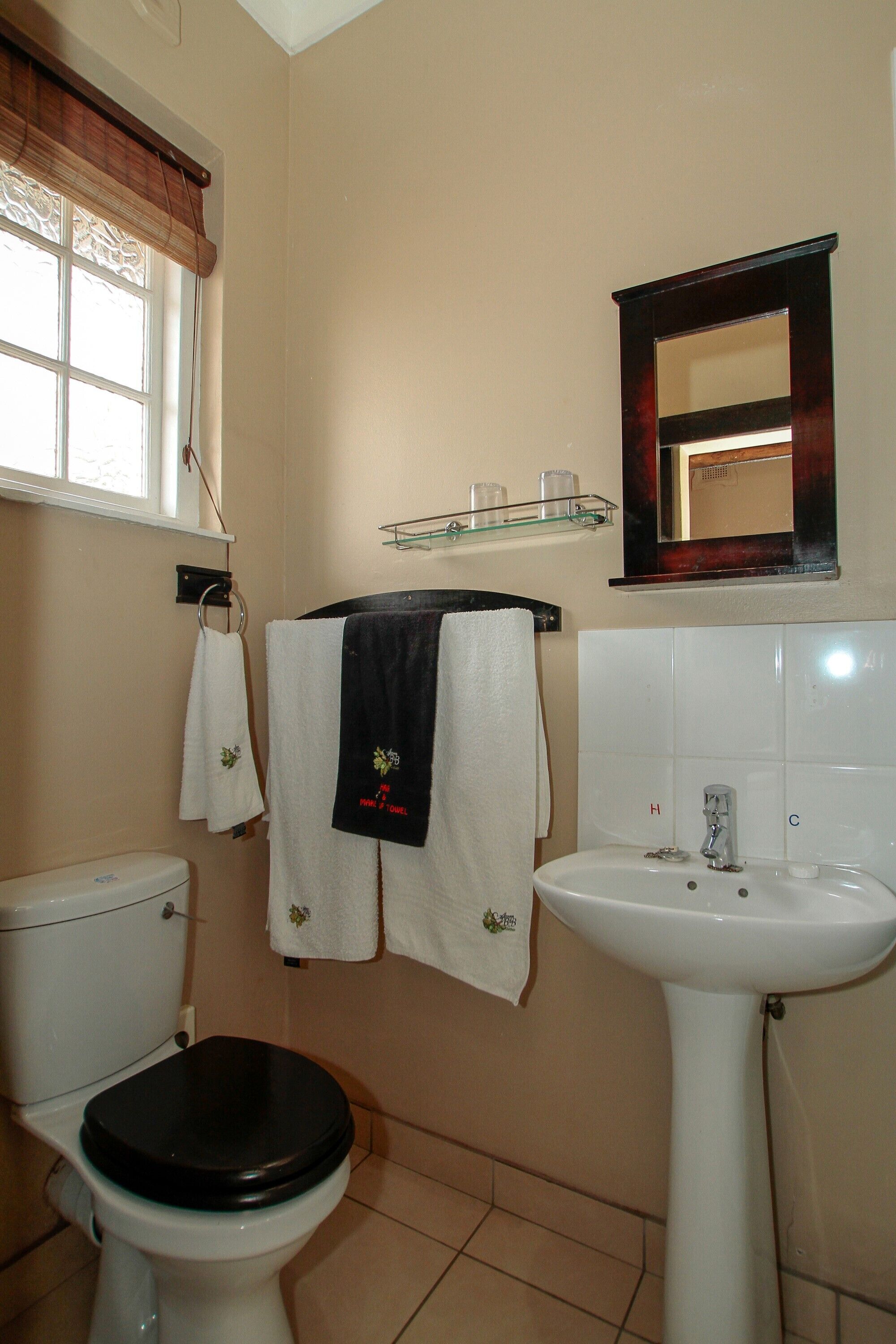 Et badeværelse med toilet, håndvask og et vindue med gardin.