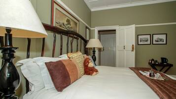 A hotel room with a bed, two lamps, a teddy bear, a brown throw blanket, and a small table with a tray.