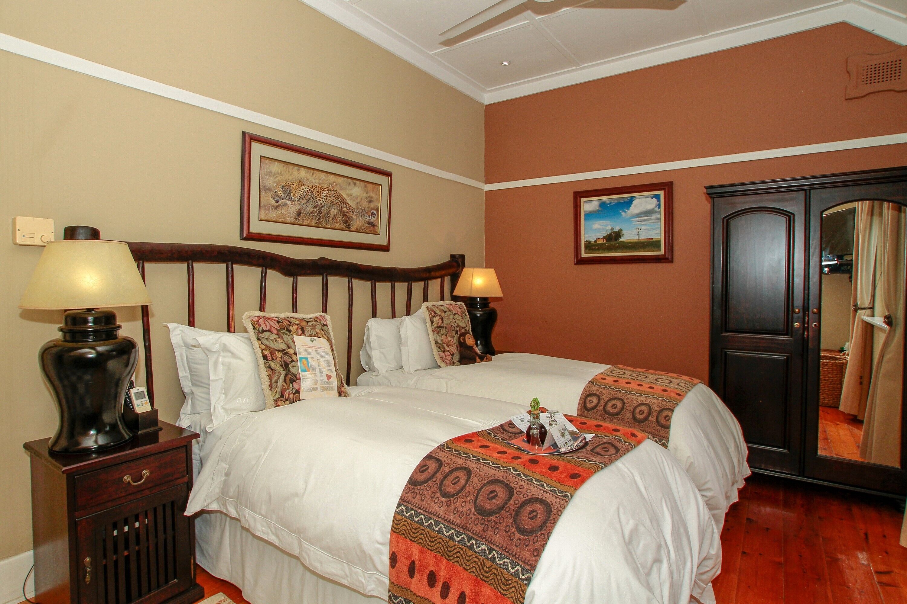A hotel room with two beds, a nightstand with a lamp, a dresser, and a mirror.