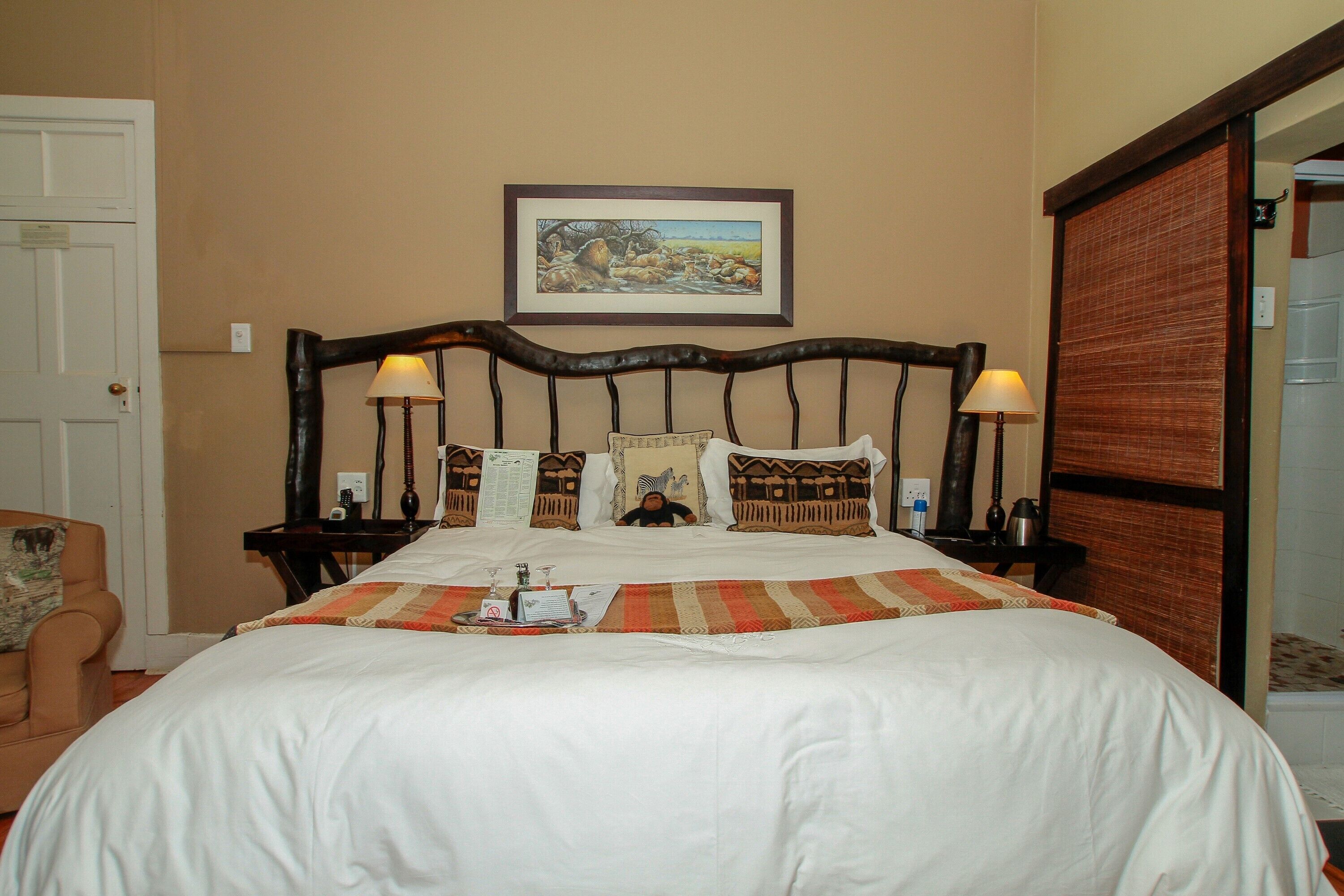 A neatly made bed with a striped bedspread, two bedside lamps, and a framed landscape painting on the wall.