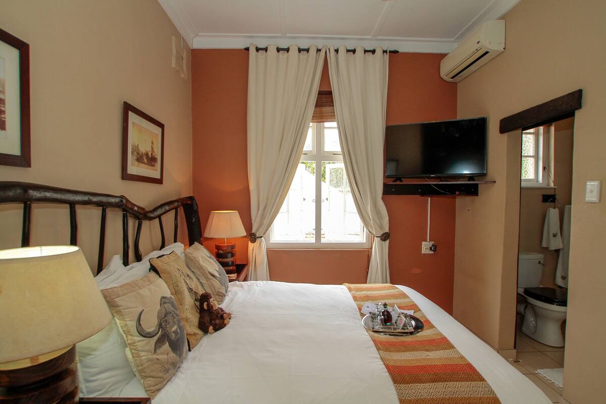 A hotel room with a bed, a television, a window with curtains, a bedside lamp, and a picture on the wall.