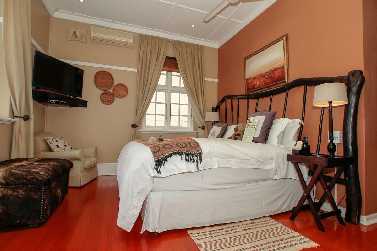 A bedroom with a bed, a television, a chair, a lamp, and a window with curtains.