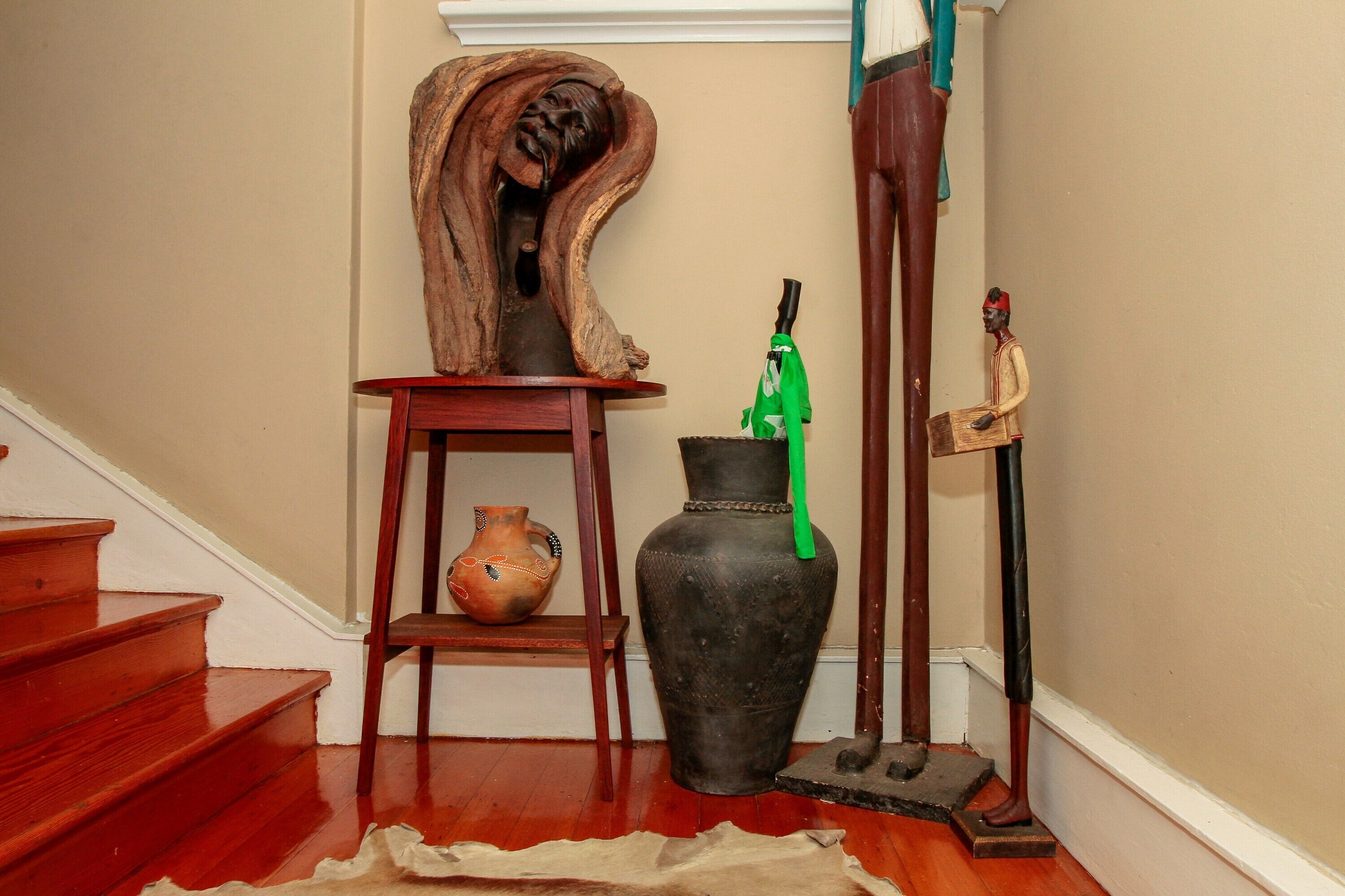 A staircase with wooden steps, a vase, a wooden sculpture, and a green umbrella.