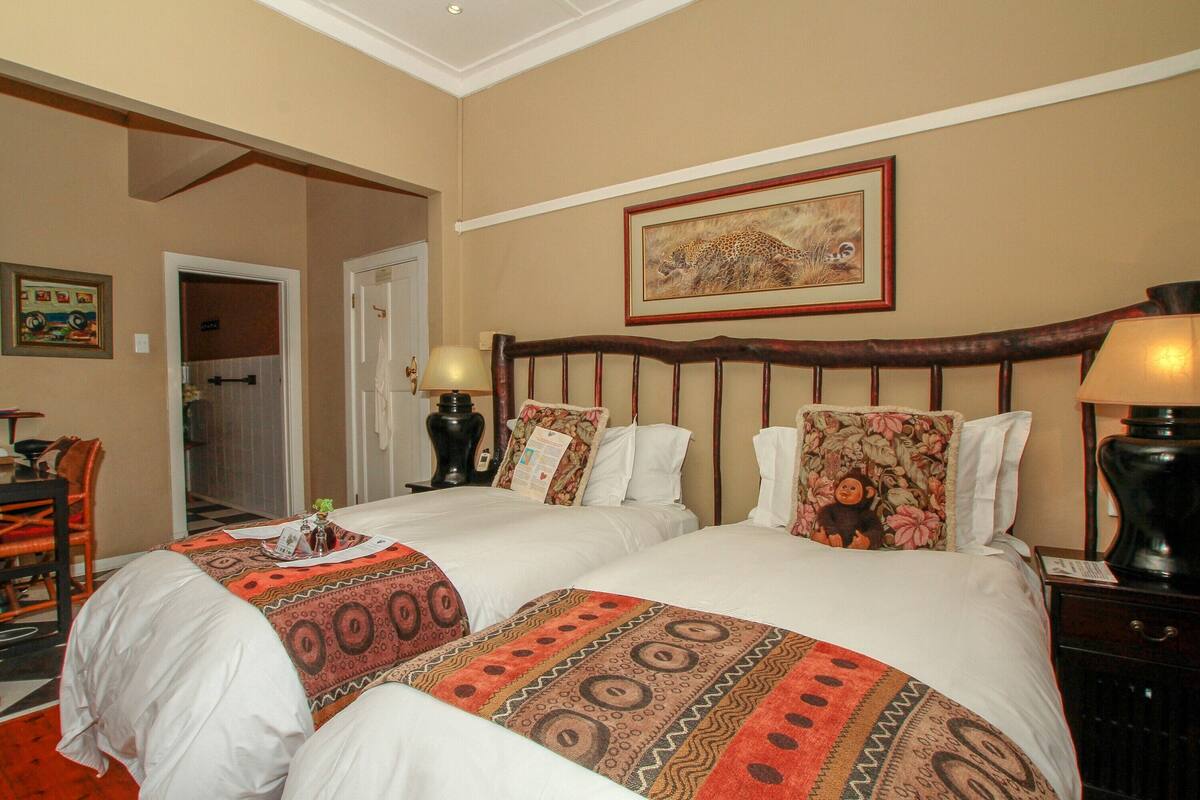 A hotel room with two beds, a painting on the wall, and a desk with a chair.