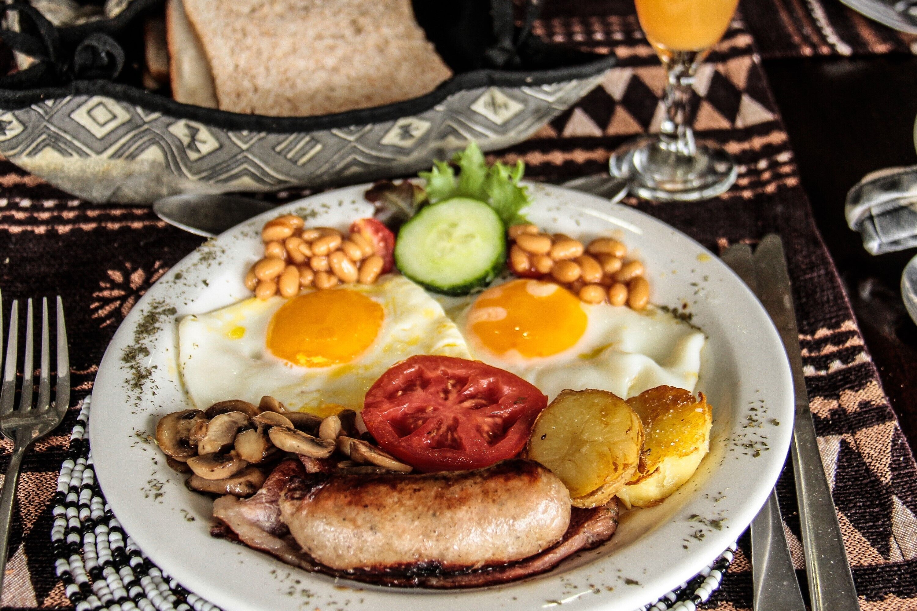 A plate of breakfast with eggs, beans, mushrooms, bacon, and tomatoes.