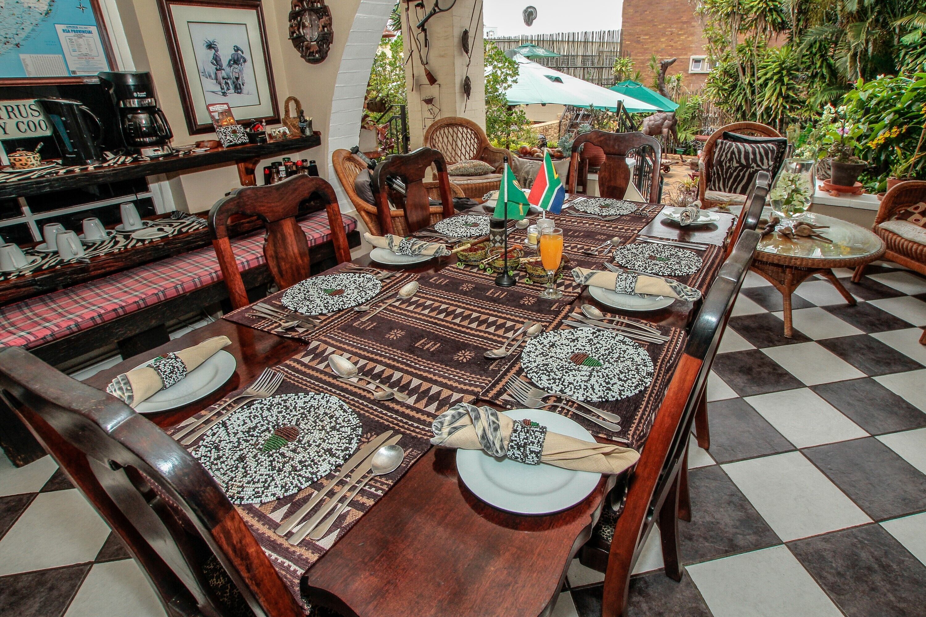 A dining area with a checkered floor, wooden chairs, and a long table set for a meal.