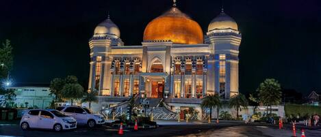A large, illuminated building with two prominent domes and a central dome, featuring a grand entrance and a staircase leading to the main doors.