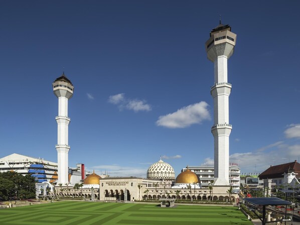 Une mosquée dotée de deux hauts minarets et de coupoles dorées, entourée d’une pelouse bien entretenue et d’immeubles modernes.