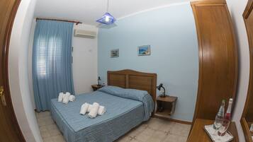 A bedroom with a bed, a nightstand, a bedside table, a lamp, a curtain, and a wall-mounted air conditioner.