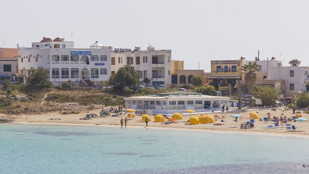 A coastal hotel with multiple floors, a beach area with umbrellas, and a clear view of the sea. - Hotel Giglio (Lampedusa)