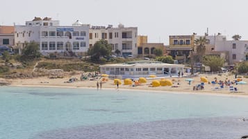 A coastal hotel with multiple floors, a beach area with umbrellas, and a clear view of the sea.