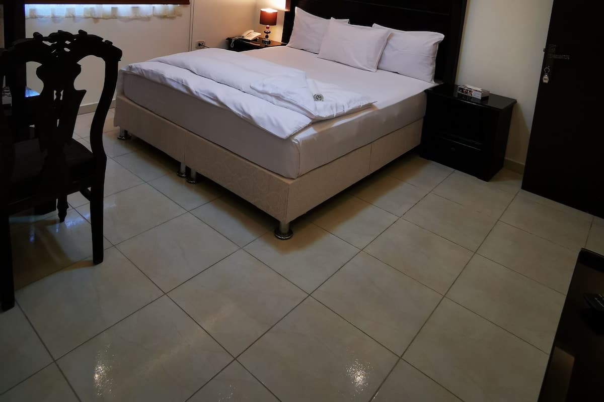 A neatly arranged bedroom with a bed, bedside table, lamp, and a chair.
