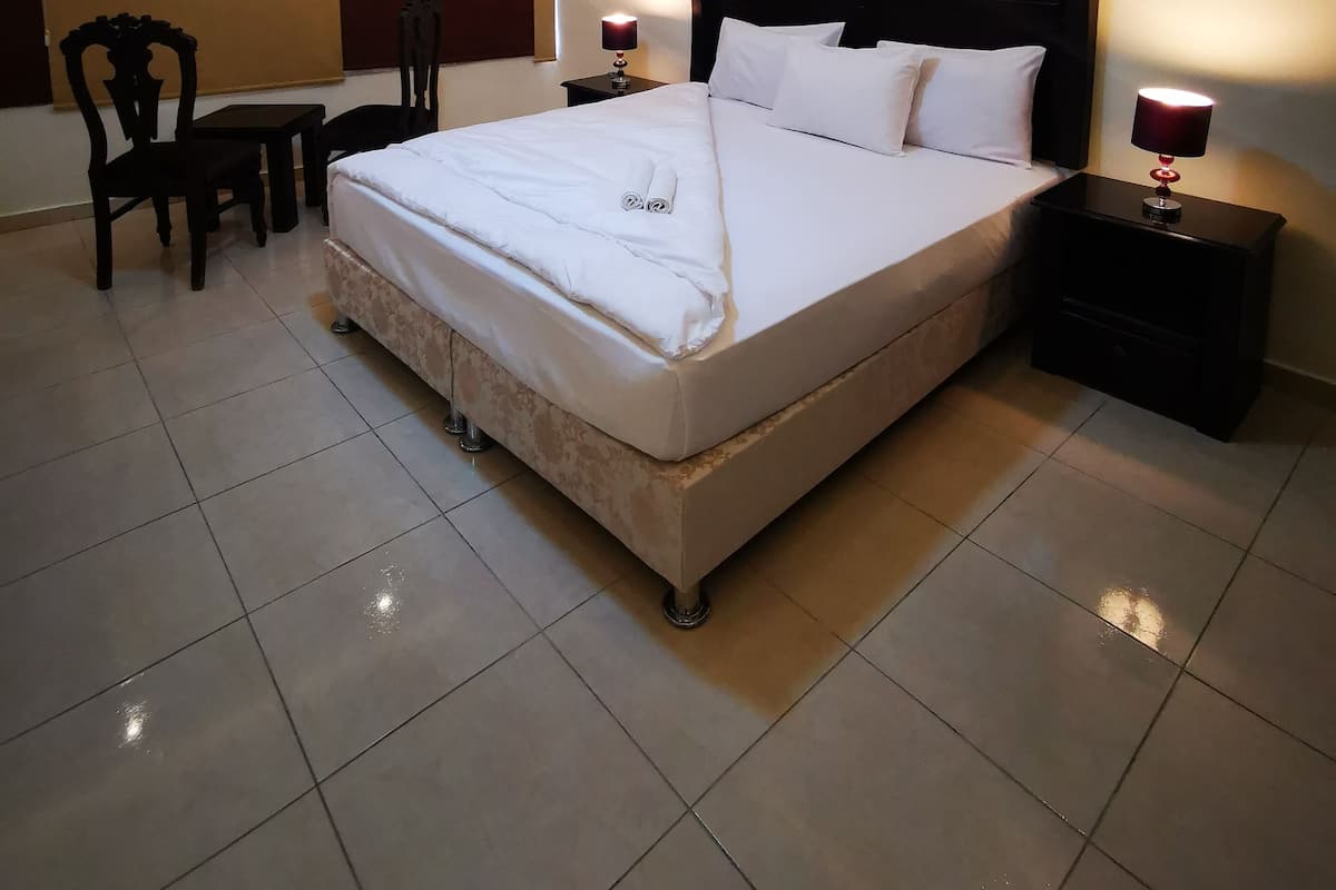A hotel room with a large bed, two bedside tables, a desk with chairs, and a ceiling light.