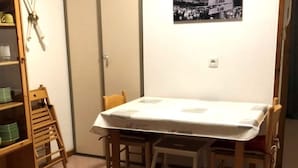 A small dining area with a table covered by a white tablecloth, surrounded by wooden chairs and a small step stool.