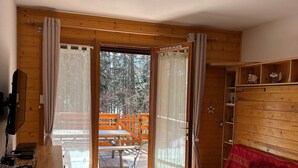A wooden interior with a sliding glass door to an outdoor deck, a red sofa, and a wooden bookshelf.