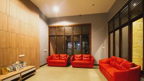Un salon moderne avec trois canapés en cuir rouge, un meuble en bois contenant des magazines et une grande fenêtre avec des stores.