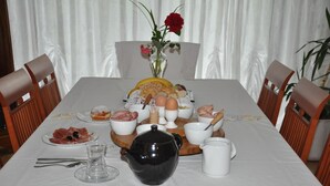 Et spisebord dækket med morgenmad, inklusive brød, æg og bagværk, med en vase blomster i baggrunden.