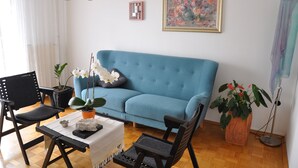 En opholdsstue med en blå sofa, et sofabord med pynteting, en sort lænestol, en potteplante og en gulvlampe.