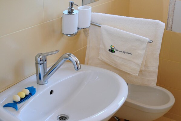 A bathroom with a white sink, a chrome faucet, a toothbrush holder, and a towel rack with a white towel. - Green Point (Brezovica)
