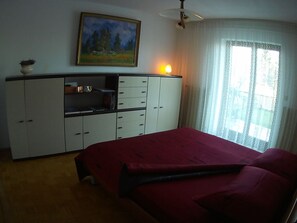 Un dormitorio con cama, armario, un cuadro y ventana con cortinas.