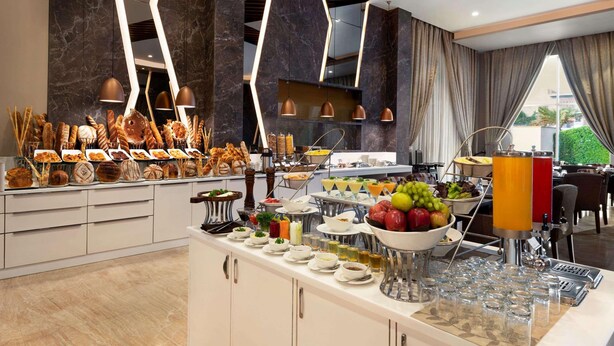 A buffet setup with various food items, a juice dispenser, and a seating area with a view. - Ramada By Wyndham Aligarh Gt Road (Aligarh)