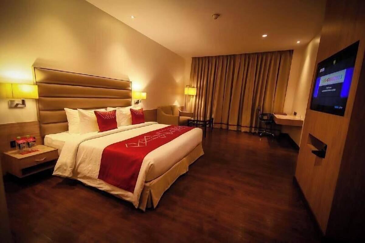 A hotel room with a large bed, bedside tables, a desk, a chair, a TV, and a curtain.