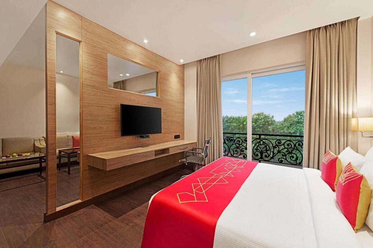 A hotel room with a large bed, a TV, a balcony with a view, and a wooden wall.