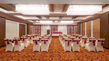 A conference room with rows of white chairs with red sashes, a patterned carpet, and a stage with a red backdrop.