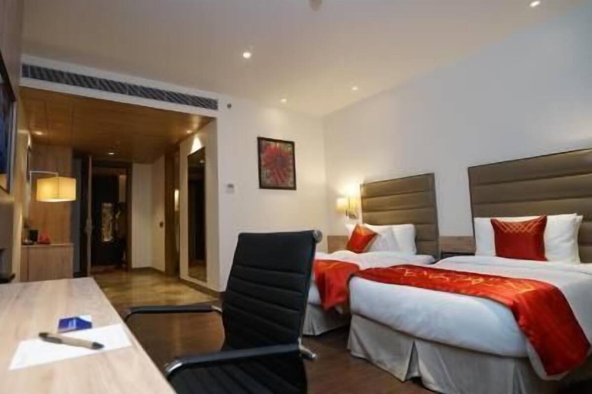 A hotel room with two beds, a desk with a chair, a lamp, and a painting on the wall.