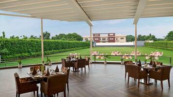 An outdoor dining area with tables and chairs, a view of a golf course, and a building in the background.