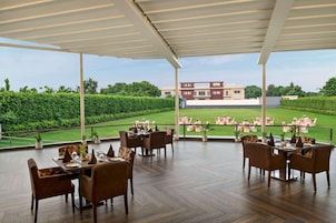 Un área de comedor al aire libre con mesas y sillas, vista a un campo de golf y un edificio al fondo.