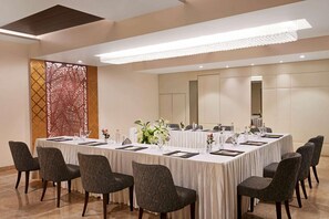 Un salón de conferencias con una larga mesa, sillas y un separador decorativo.
