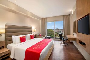A hotel room with a large bed, a desk, a chair, and a TV.