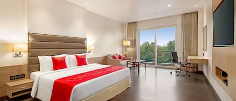 A hotel room with a large bed, a desk, a chair, a TV, and a balcony with a view.