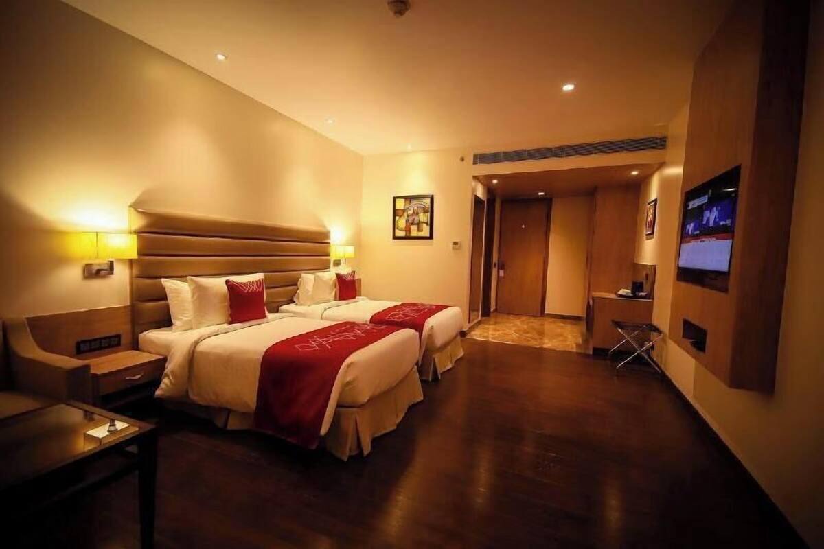 A hotel room with two beds, a desk, a TV, and a door leading to another room.