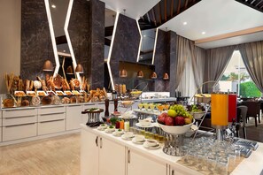 A buffet setup with various food items, a juice dispenser, and a seating area with a view. - Ramada By Wyndham Aligarh Gt Road (Aligarh)