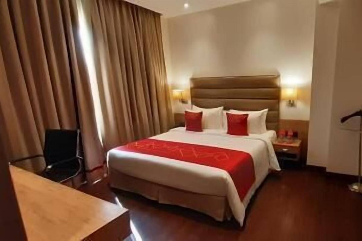 A hotel room with a large bed, a desk, a chair, a nightstand, and a floor lamp.