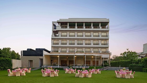 A multi-story hotel with a flat roof, balconies, and a well-maintained lawn with tables and chairs.